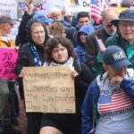 A woman holds a sign that reads, "When the Lawmakers are the Lawbreakers There is No Law."
